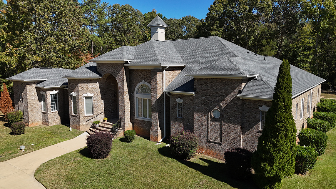 A large, elegant brick home with a gray shingle roof, multiple gables, and a small cupola on top.